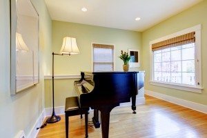 Green living room with black piano and large window.